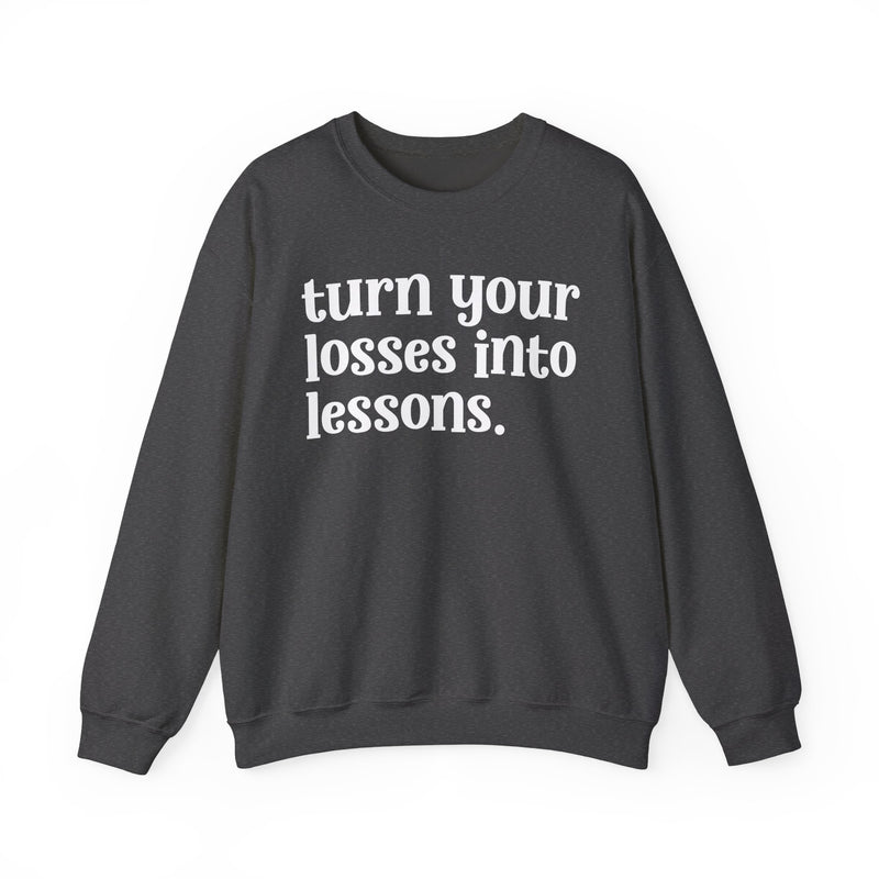 Dark heather crewneck sweatshirt with white "turn your losses into lessons." lettering, front view.