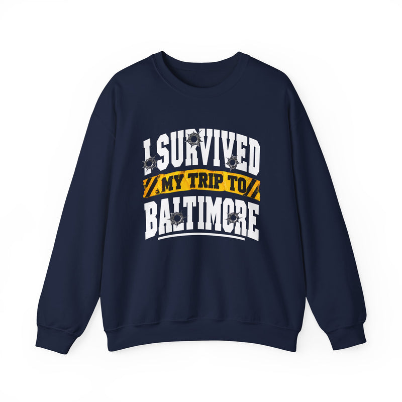 Navy sweatshirt with white block lettering reading I SURVIVED MY TRIP TO BALTIMORE, with bullet-hole accents and a yellow caution-tape banner, front flat-lay view.