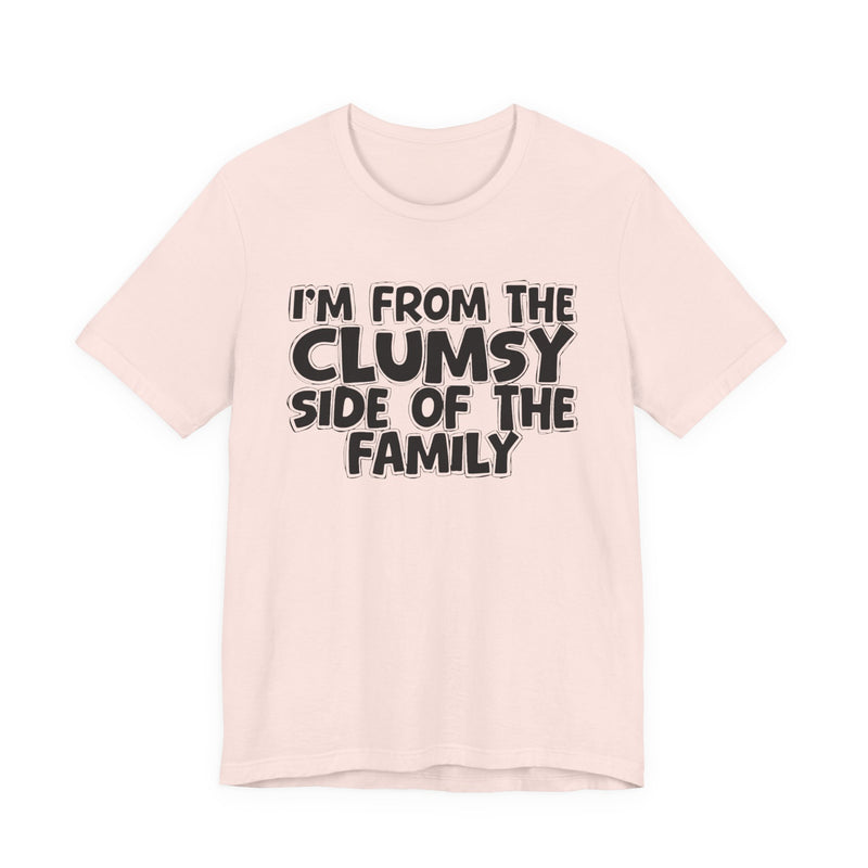 Soft Pink t-shirt, printed with the "I'M FROM THE CLUMSY SIDE OF THE FAMILY" statement in bold outlined bubble lettering, front flat-lay view.