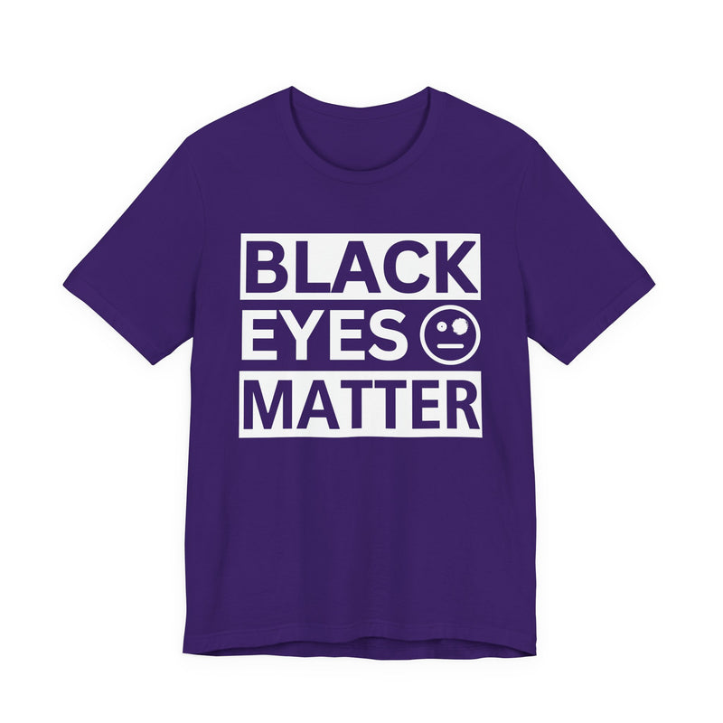 Navy t-shirt with ‘BLACK EYES MATTER’ in boxed block lettering with a smiley-face eye icon graphic in light-contrast print, front flat-lay mockup view