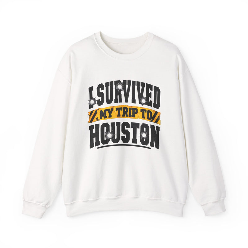 White sweatshirt with black block lettering reading I SURVIVED MY TRIP TO HOUSTON, with bullet-hole accents and a yellow caution-tape banner, front flat-lay view.