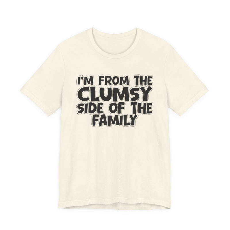 Natural t-shirt, printed with the "I'M FROM THE CLUMSY SIDE OF THE FAMILY" statement in bold outlined bubble lettering, front flat-lay view.