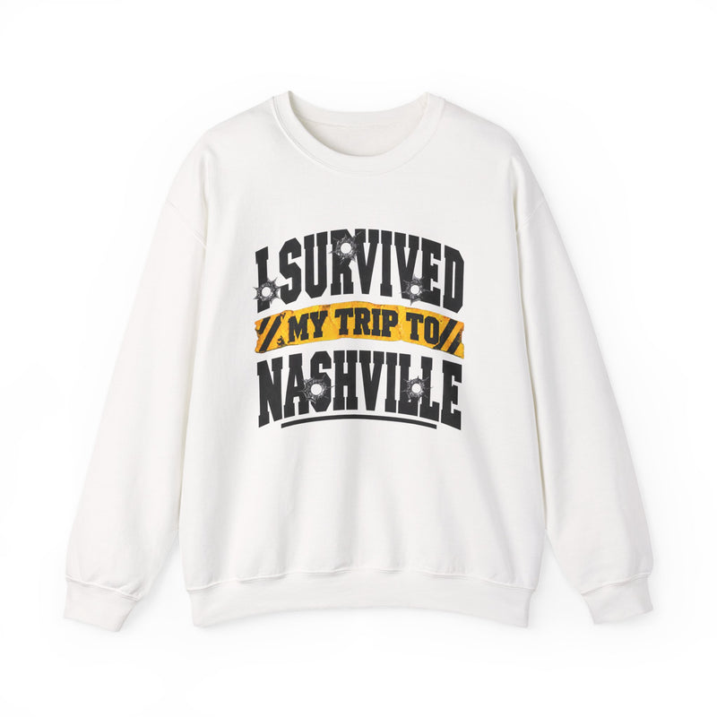 White sweatshirt with black block lettering reading I SURVIVED MY TRIP TO NASHVILLE, with bullet-hole accents and a yellow caution-tape banner, front flat-lay view.
