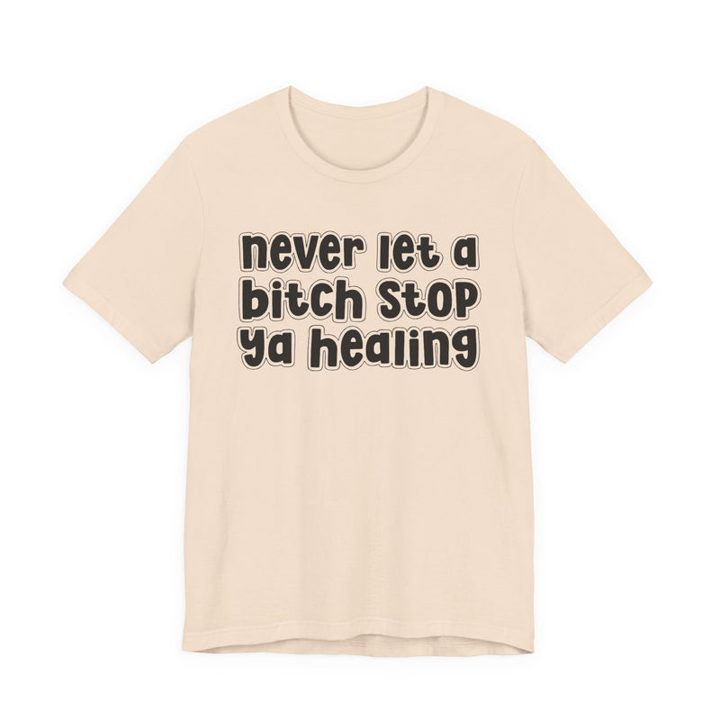 Graphic t-shirt with bold statement lettering reading "NEVER LET A BITCH STOP YA HEALING", front view, product mockup