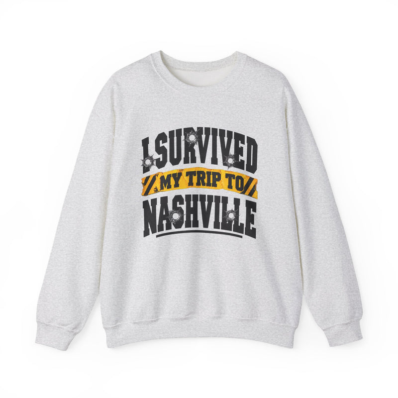 White sweatshirt with black block lettering reading I SURVIVED MY TRIP TO NASHVILLE, with bullet-hole accents and a yellow caution-tape banner, front flat-lay view.