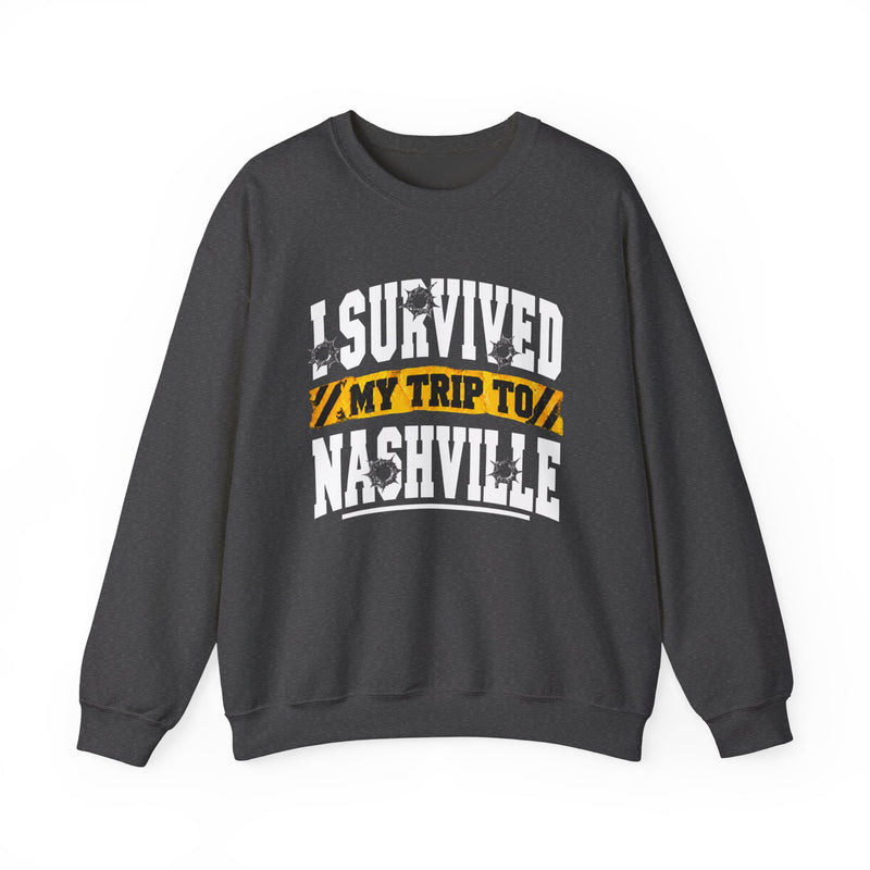 Charcoal sweatshirt with white block lettering reading I SURVIVED MY TRIP TO NASHVILLE, with bullet-hole accents and a yellow caution-tape banner, front flat-lay view.