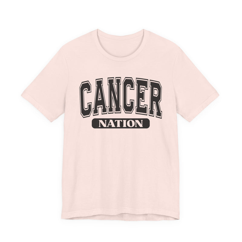 Soft pink t-shirt with black arched CANCER collegiate lettering over a white NATION pill badge, front flat-lay view.