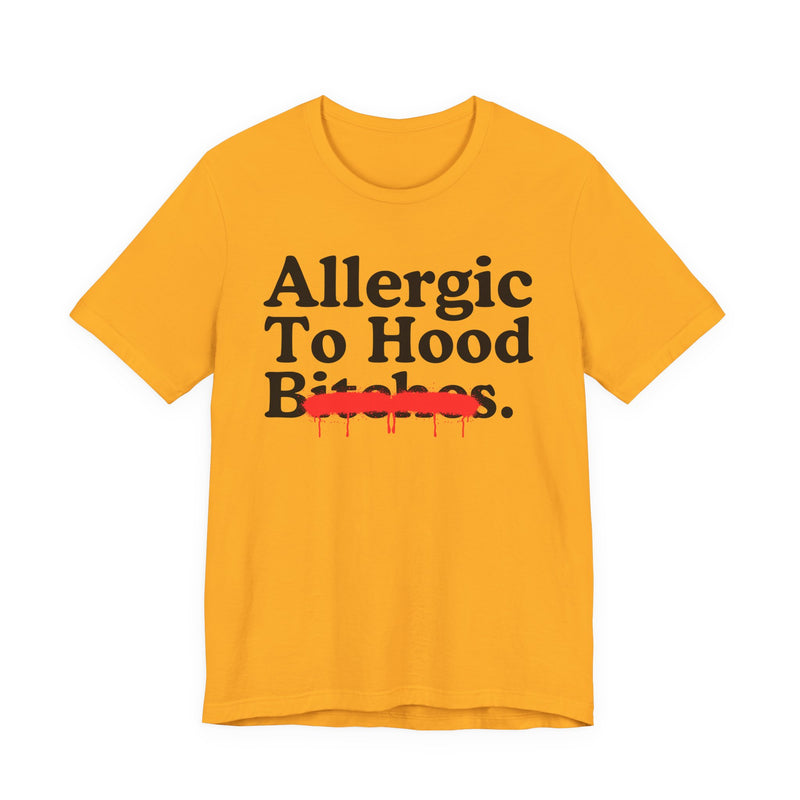 Gold T-Shirt with serif lettering reading Allergic To Hood Bitches, crossed by a red dripping strikethrough, front flat-lay view.