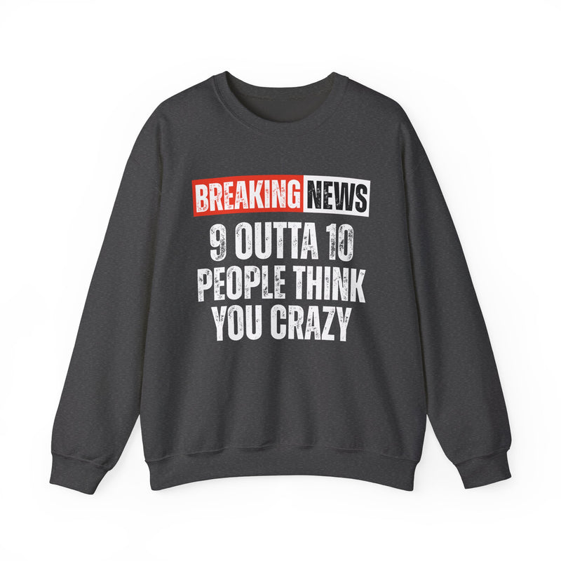 BREAKING NEWS banner graphic with distressed headline text '9 OUTTA 10 PEOPLE THINK YOU CRAZY' - sweatshirt in charcoal, front view, product mockup on white background