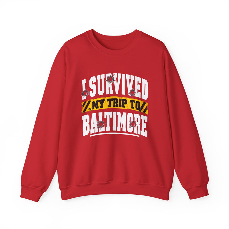Red sweatshirt with white block lettering reading I SURVIVED MY TRIP TO BALTIMORE, with bullet-hole accents and a yellow caution-tape banner, front flat-lay view.