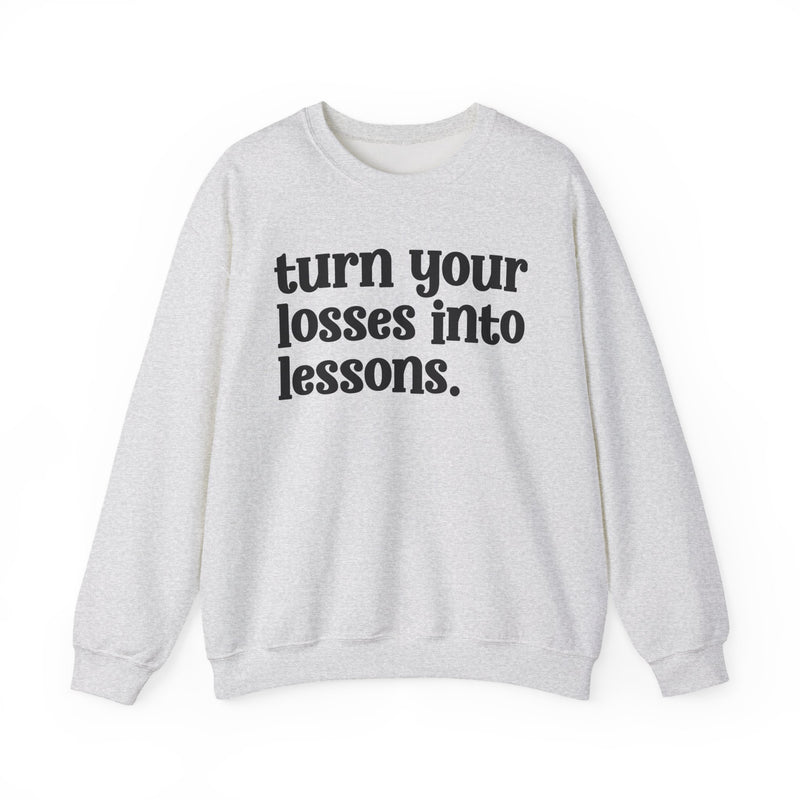 Heather white crewneck sweatshirt with black "turn your losses into lessons." lettering, front view.