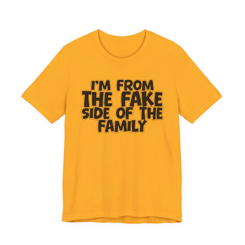 Olive t-shirt with "I'M FROM THE FAKE SIDE OF THE FAMILY" in bold white outlined bubble lettering, front flat-lay view