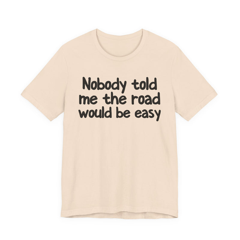 T-Shirt with text design reading “NOBODY TOLD ME THE ROAD WOULD BE EASY”, front view