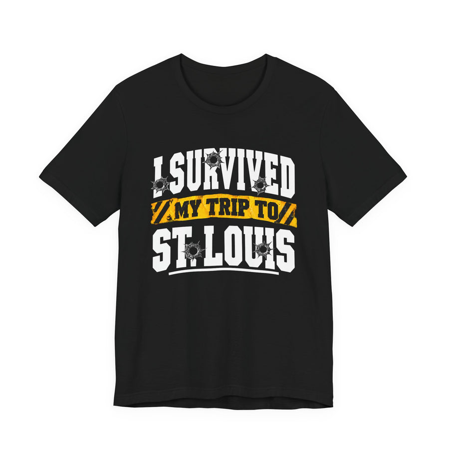 Black t-shirt with white block lettering reading I SURVIVED MY TRIP TO ST. LOUIS, with bullet-hole accents and a yellow caution-tape banner, front flat-lay view.