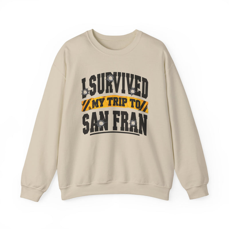 Sand sweatshirt with black block lettering reading I SURVIVED MY TRIP TO BALTIMORE, with bullet-hole accents and a yellow caution-tape banner, front flat-lay view.
