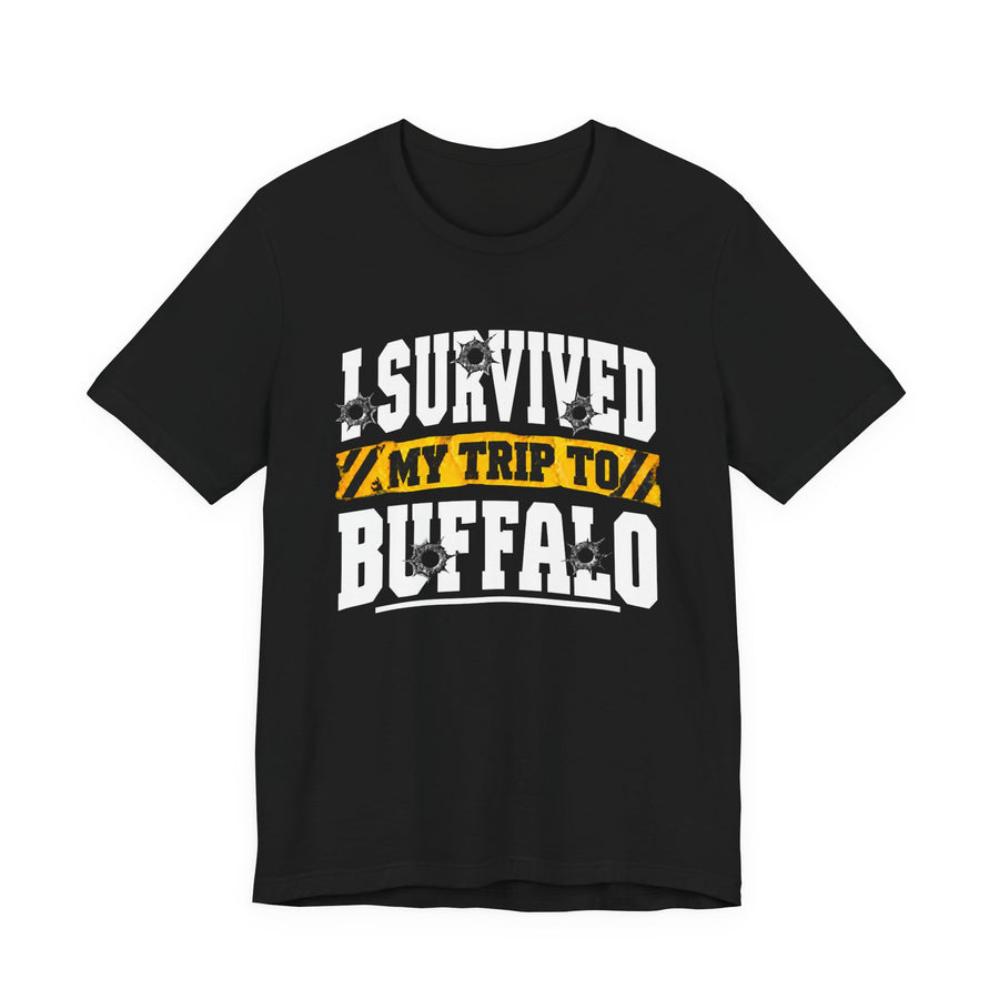 T-Shirt product photo with arched collegiate lettering reading "I SURVIVED" with bullet-hole decals, a caution-tape band reading "MY TRIP TO", and large block letters reading "BUFFALO", front view.
