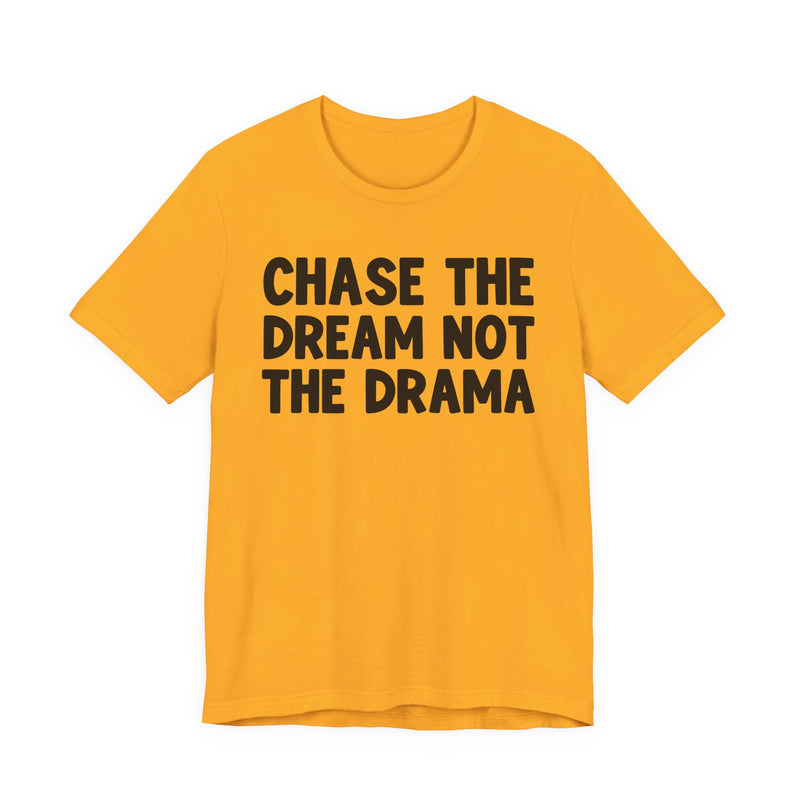 Gold t-shirt with black bold statement lettering reading CHASE THE DREAM NOT THE DRAMA, front flat-lay view.