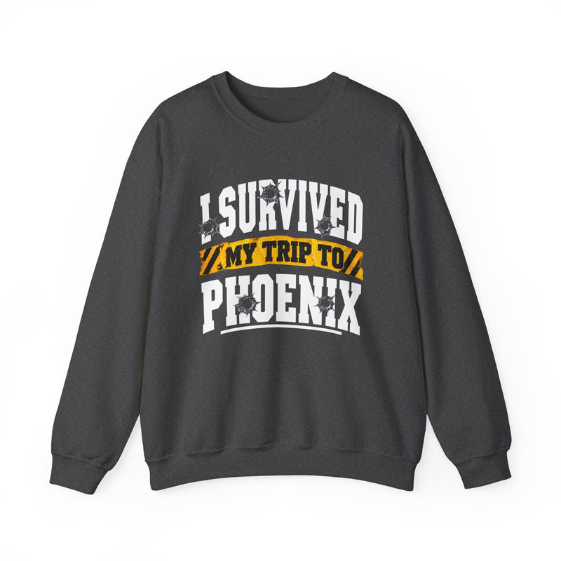 Charcoal sweatshirt with white block lettering reading I SURVIVED MY TRIP TO PHOENIX, with bullet-hole accents and a yellow caution-tape banner, front flat-lay view.