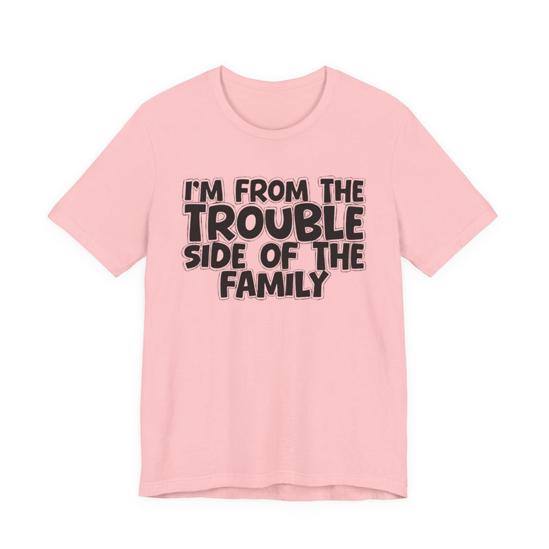 Pink t-shirt, printed with the "I'M FROM THE TROUBLE SIDE OF THE FAMILY" statement in bold outlined bubble lettering, front flat-lay view.