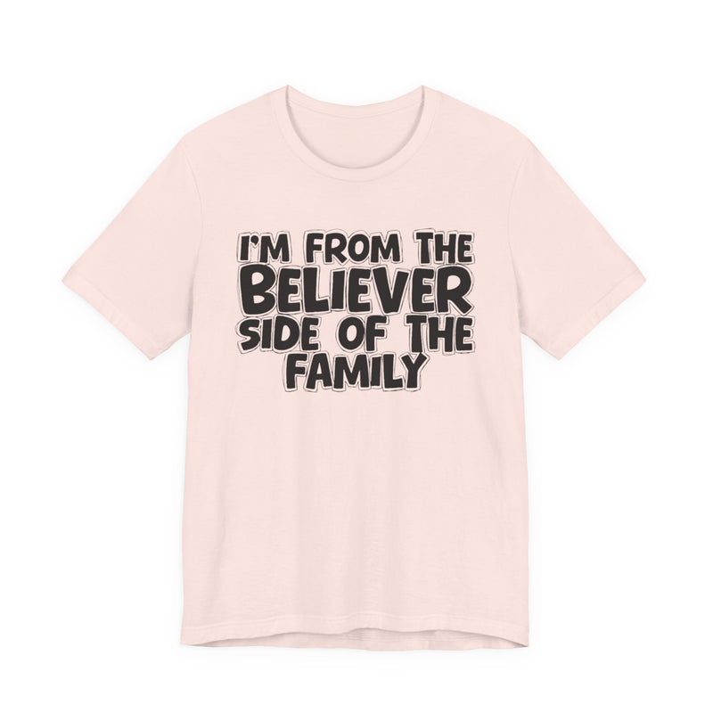 Soft Pink t-shirt with white outlined bubble lettering reading 'I'M FROM THE BELIEVER SIDE OF THE FAMILY', front flat-lay view.