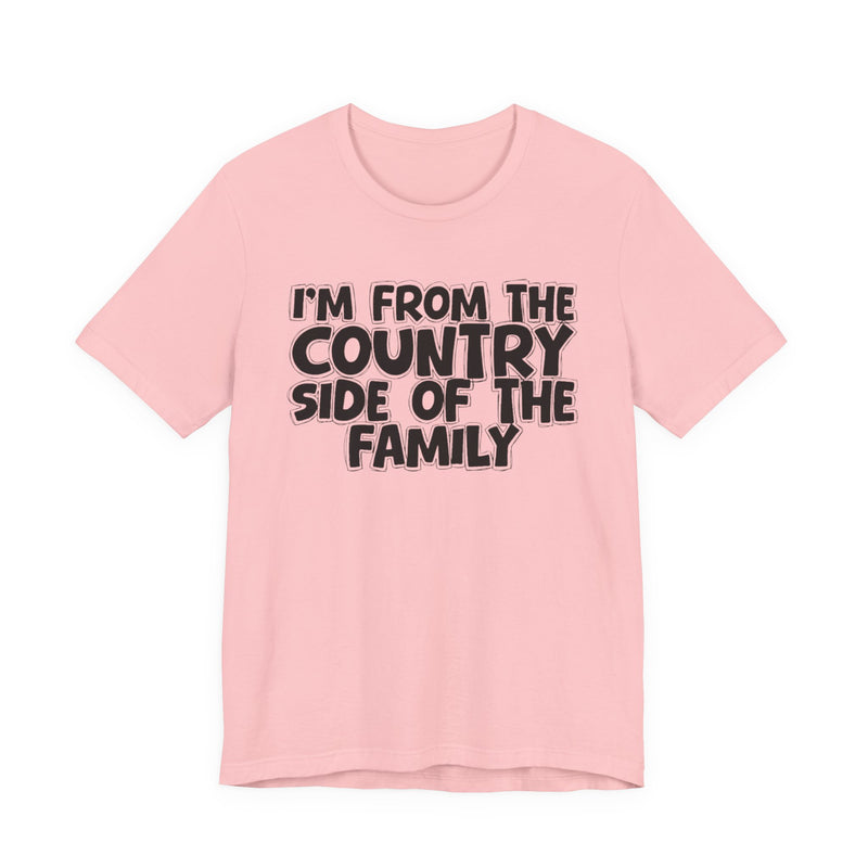 Pink t-shirt with white outlined bubble lettering reading 'I'M FROM THE COUNTRY SIDE OF THE FAMILY', front flat-lay view.