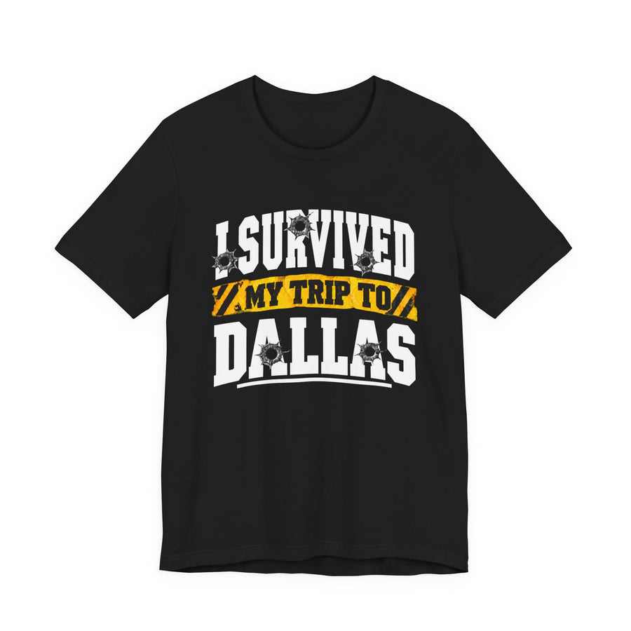 T-Shirt product photo with arched collegiate lettering reading "I SURVIVED" with bullet-hole decals, a caution-tape band reading "MY TRIP TO", and large block letters reading "DALLAS", front view.