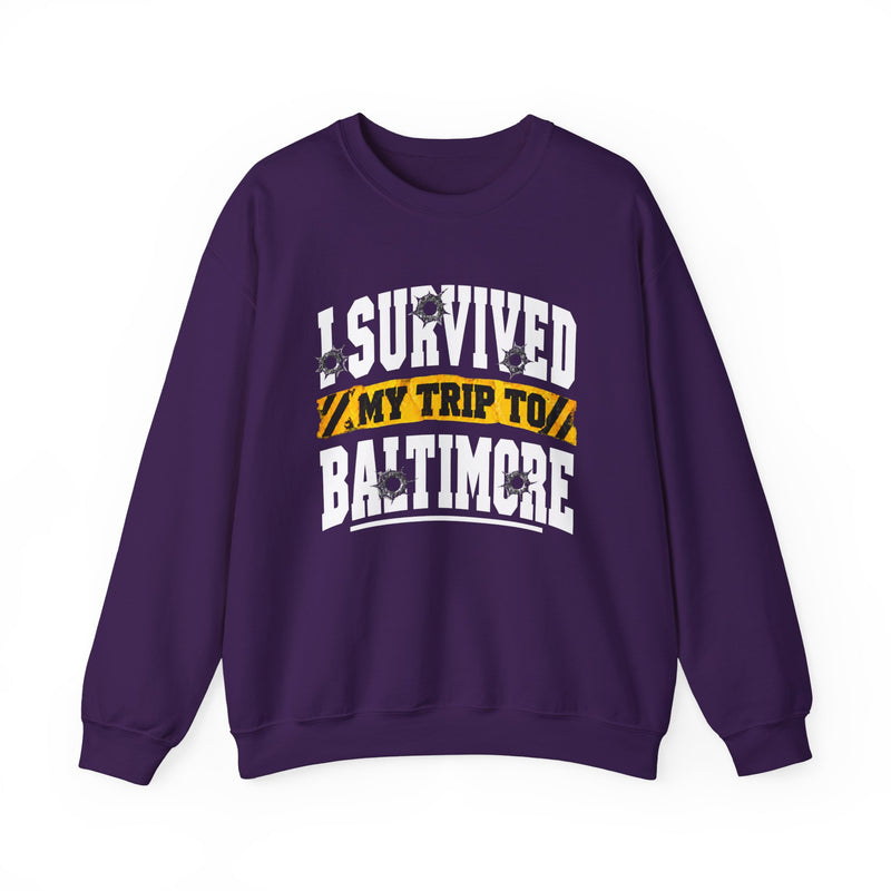 Purple sweatshirt with white block lettering reading I SURVIVED MY TRIP TO BALTIMORE, with bullet-hole accents and a yellow caution-tape banner, front flat-lay view.
