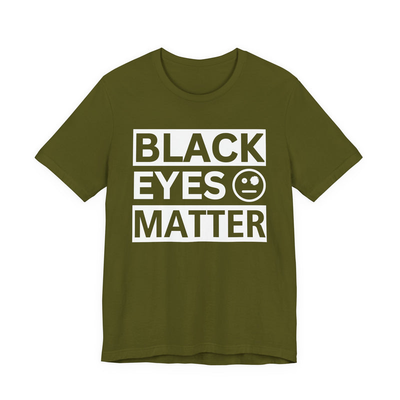 Olive t-shirt with ‘BLACK EYES MATTER’ in boxed block lettering with a smiley-face eye icon graphic in light-contrast print, front flat-lay mockup view