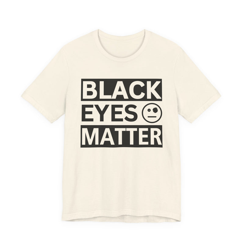 White t-shirt with ‘BLACK EYES MATTER’ in boxed block lettering with a smiley-face eye icon graphic in dark-contrast print, front flat-lay mockup view