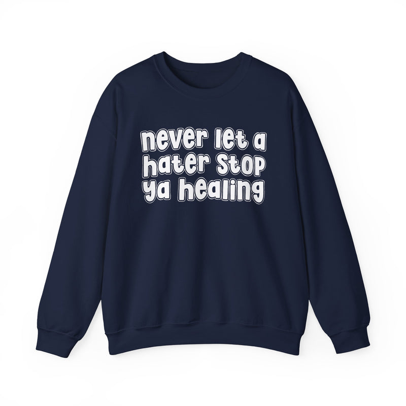 Heather navy sweatshirt with dark bold healing-journey lettering reading NEVER LET A HATER STOP YA HEALING, front flat-lay view.
