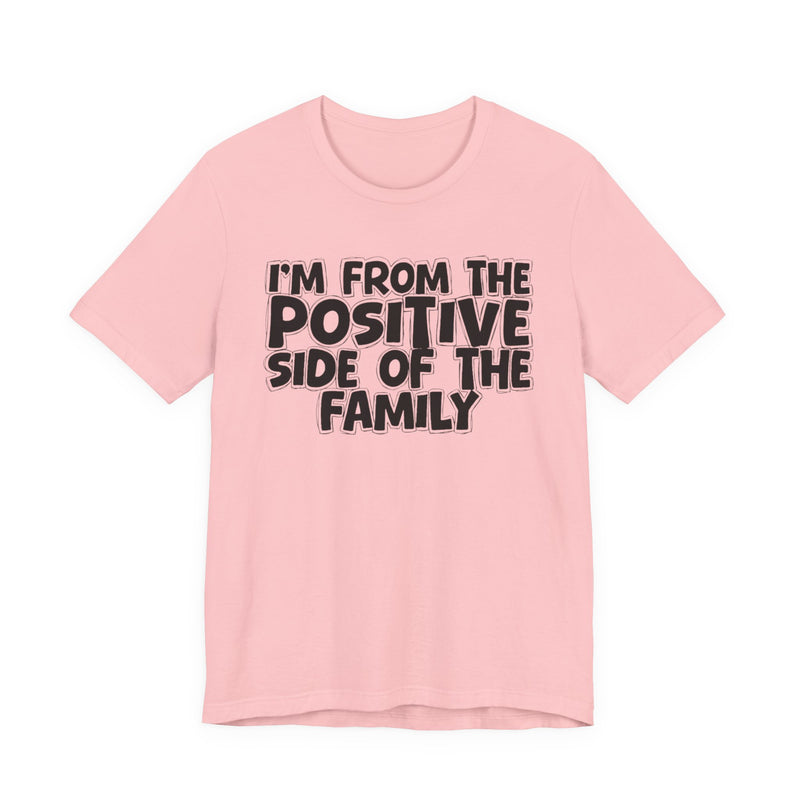 Pink t-shirt with white outlined bubble lettering reading 'I'M FROM THE POSITIVE SIDE OF THE FAMILY', front flat-lay view.