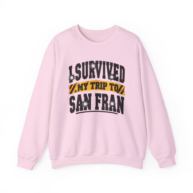Light pink sweatshirt with black block lettering reading I SURVIVED MY TRIP TO BALTIMORE, with bullet-hole accents and a yellow caution-tape banner, front flat-lay view.