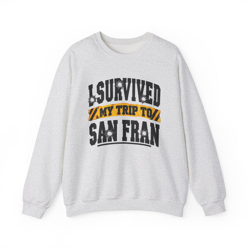 White sweatshirt with black block lettering reading I SURVIVED MY TRIP TO BALTIMORE, with bullet-hole accents and a yellow caution-tape banner, front flat-lay view.