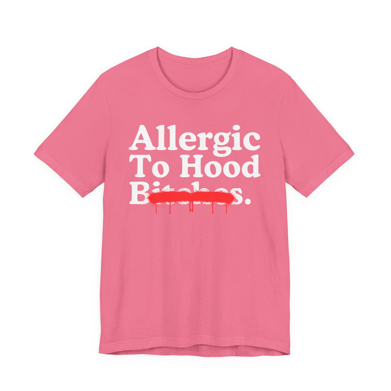 Charity Pink T-Shirt with serif lettering reading Allergic To Hood Bitches, crossed by a red dripping strikethrough, front flat-lay view.