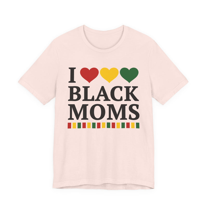 Front flat-lay of the I Love Black Moms t-shirt in Soft Pink: black 'I' with red, gold, and green hearts above black 'BLACK MOMS' collegiate lettering, with a red, gold, and green stripe bar beneath the text.