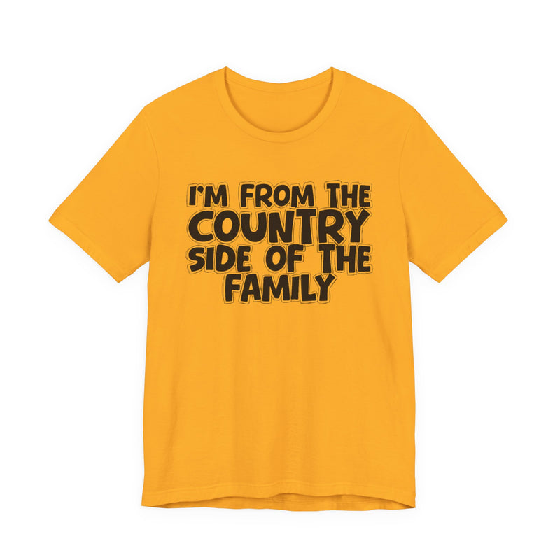 Gold t-shirt with white outlined bubble lettering reading 'I'M FROM THE COUNTRY SIDE OF THE FAMILY', front flat-lay view.