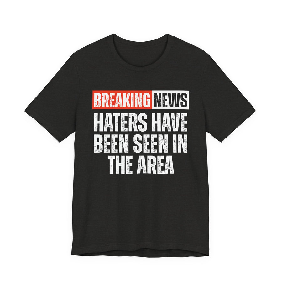 BREAKING NEWS: HATERS HAVE BEEN SEEN IN THE AREA distressed news-bar text design — t-shirt in Pepper, front view, product mockup on white background
