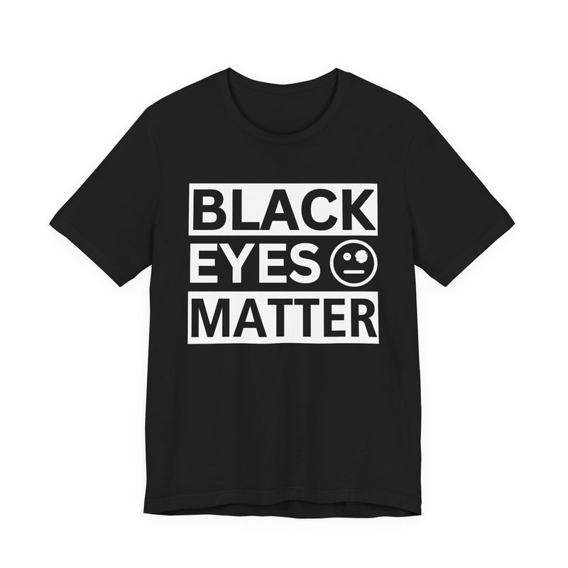 Black t-shirt with ‘BLACK EYES MATTER’ in boxed block lettering with a smiley-face eye icon graphic in light-contrast print, front flat-lay mockup view
