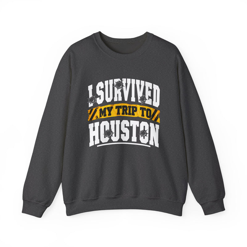 Charcoal sweatshirt with white block lettering reading I SURVIVED MY TRIP TO HOUSTON, with bullet-hole accents and a yellow caution-tape banner, front flat-lay view.