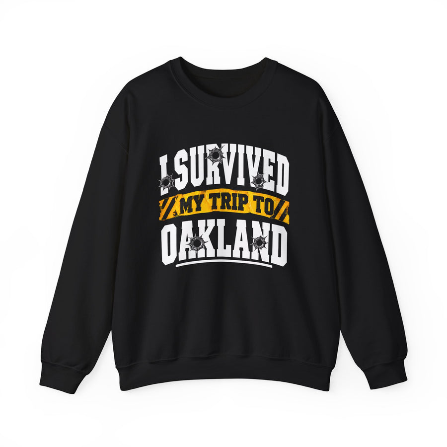Sweatshirt product photo with arched collegiate lettering reading "I SURVIVED" with bullet-hole decals, a caution-tape band reading "MY TRIP TO", and large block letters reading "OAKLAND", front view.